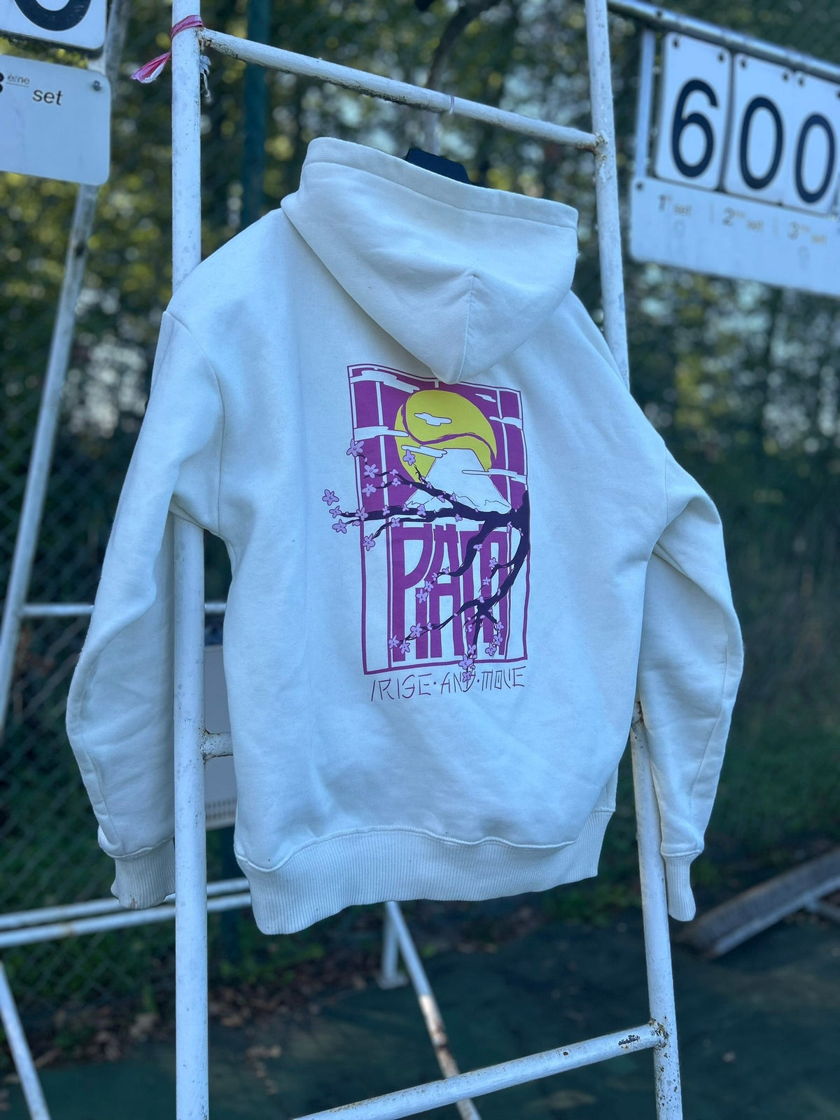 Hoodie crème /RAM à imprimé padel violet sur un portant en extérieur